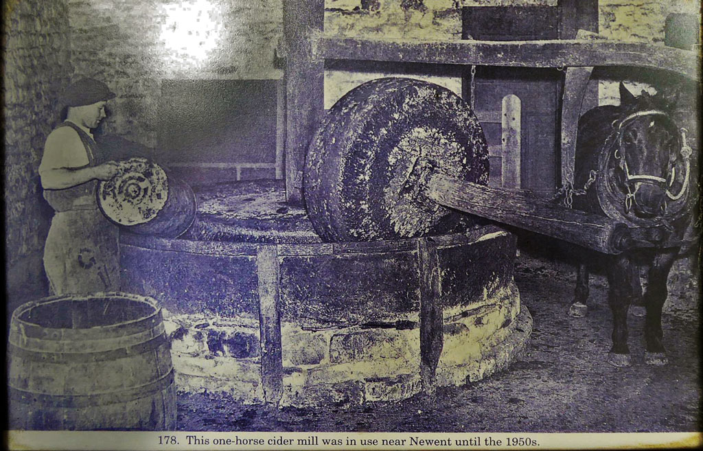 A photo of a stone cider mill with horse and mill operator.